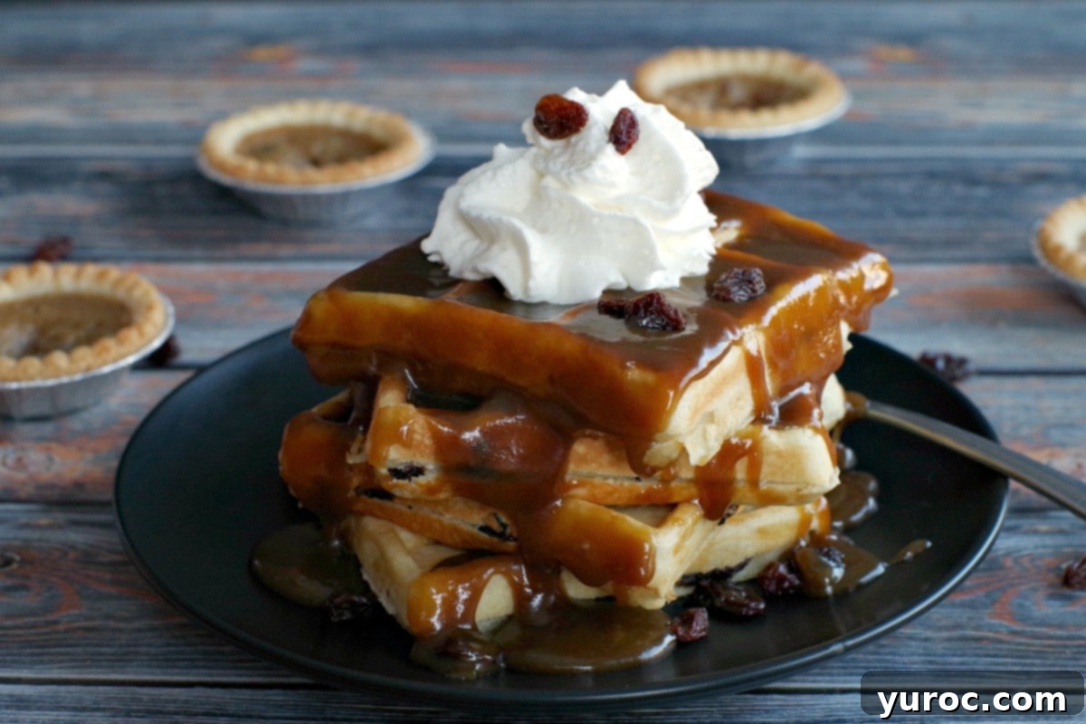 4 Butter Tart Waffles stacked on a black plate (with lots of sauce on them) on a blue wooden background and butter tarts in the background