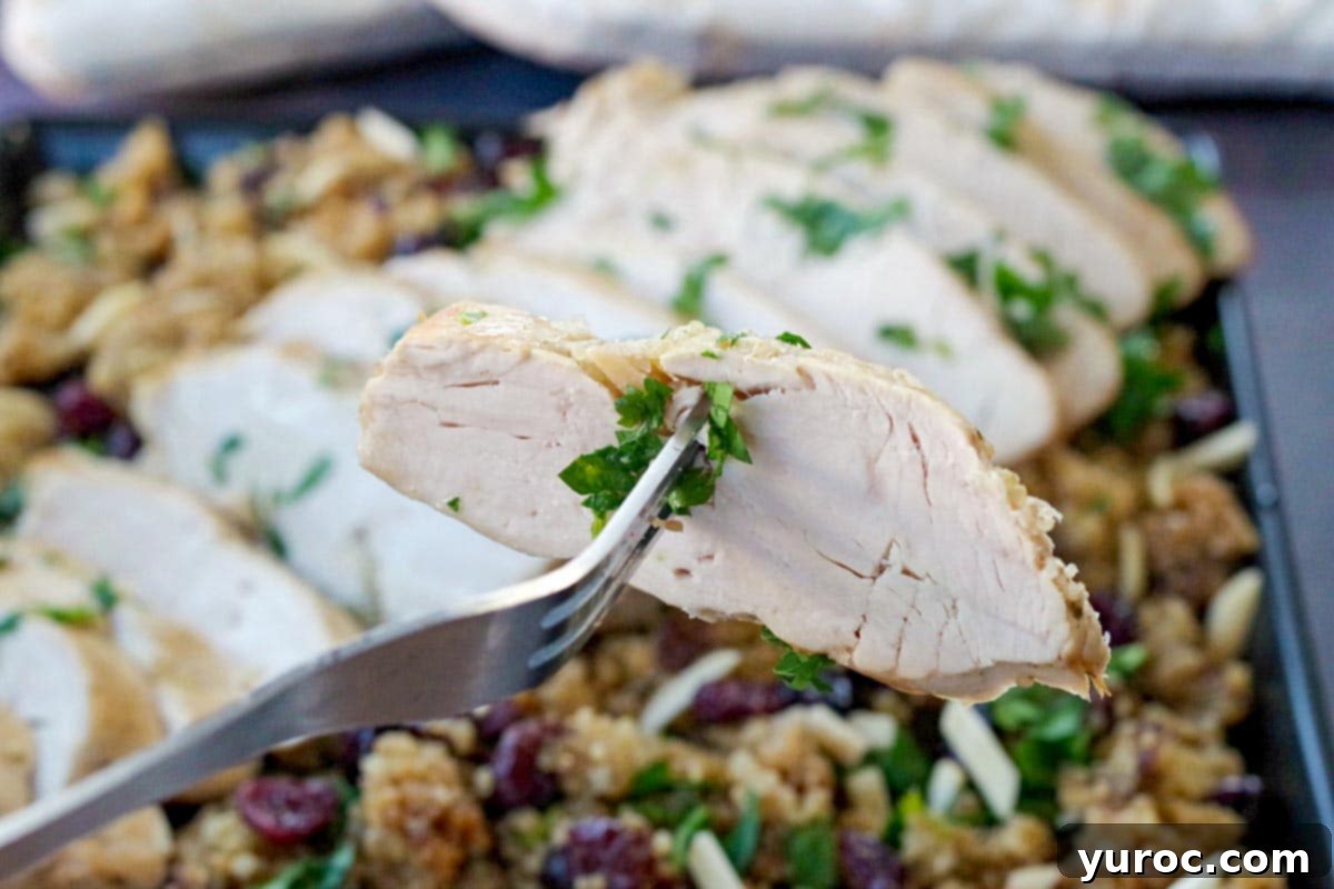 Piece of turkey breast being held up on a fork, over a platter of sliced turkey breast on cranberry quinoa dressing.