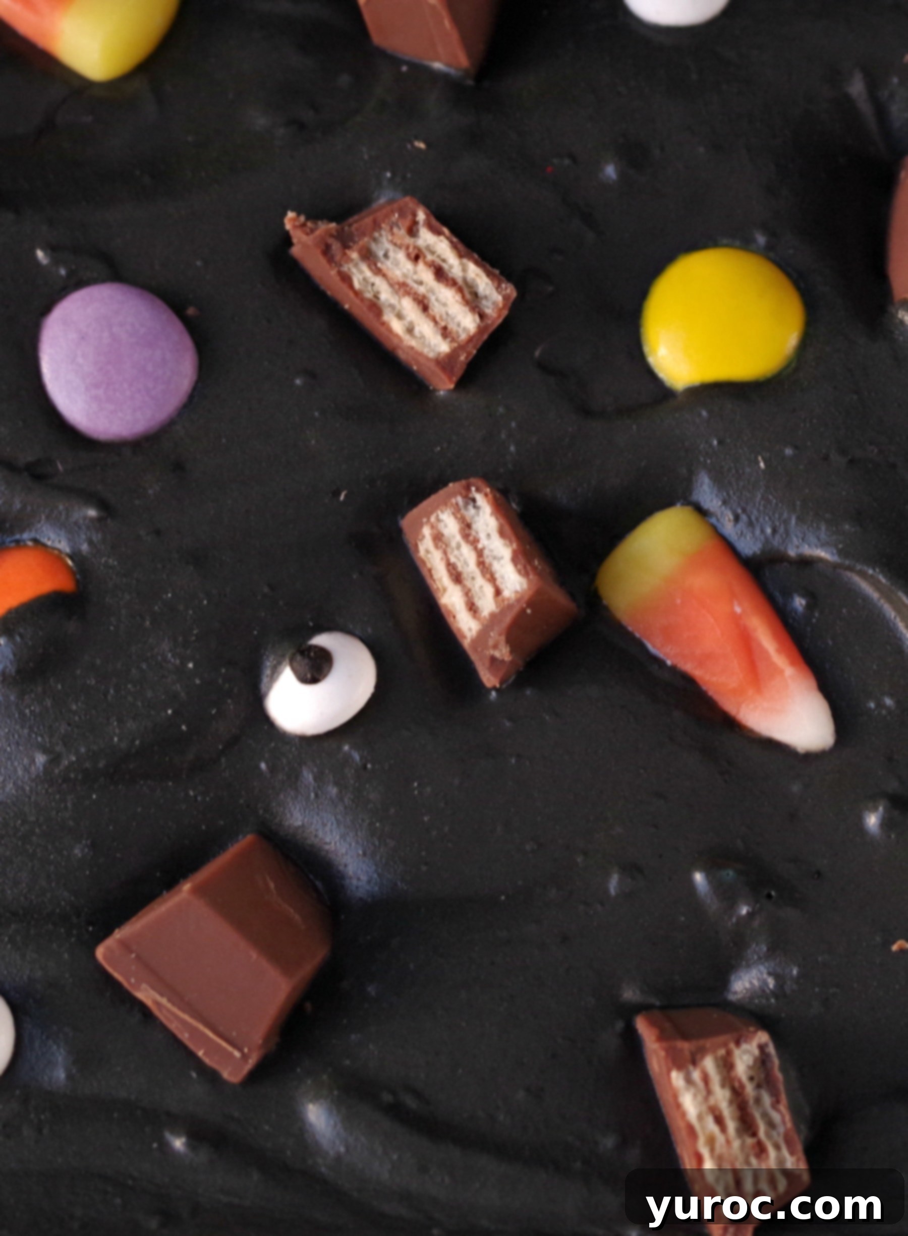 Boo batter ice cream close up. It's a black ice cream with candy eyes, candy corn, chocolate bars and smarties.