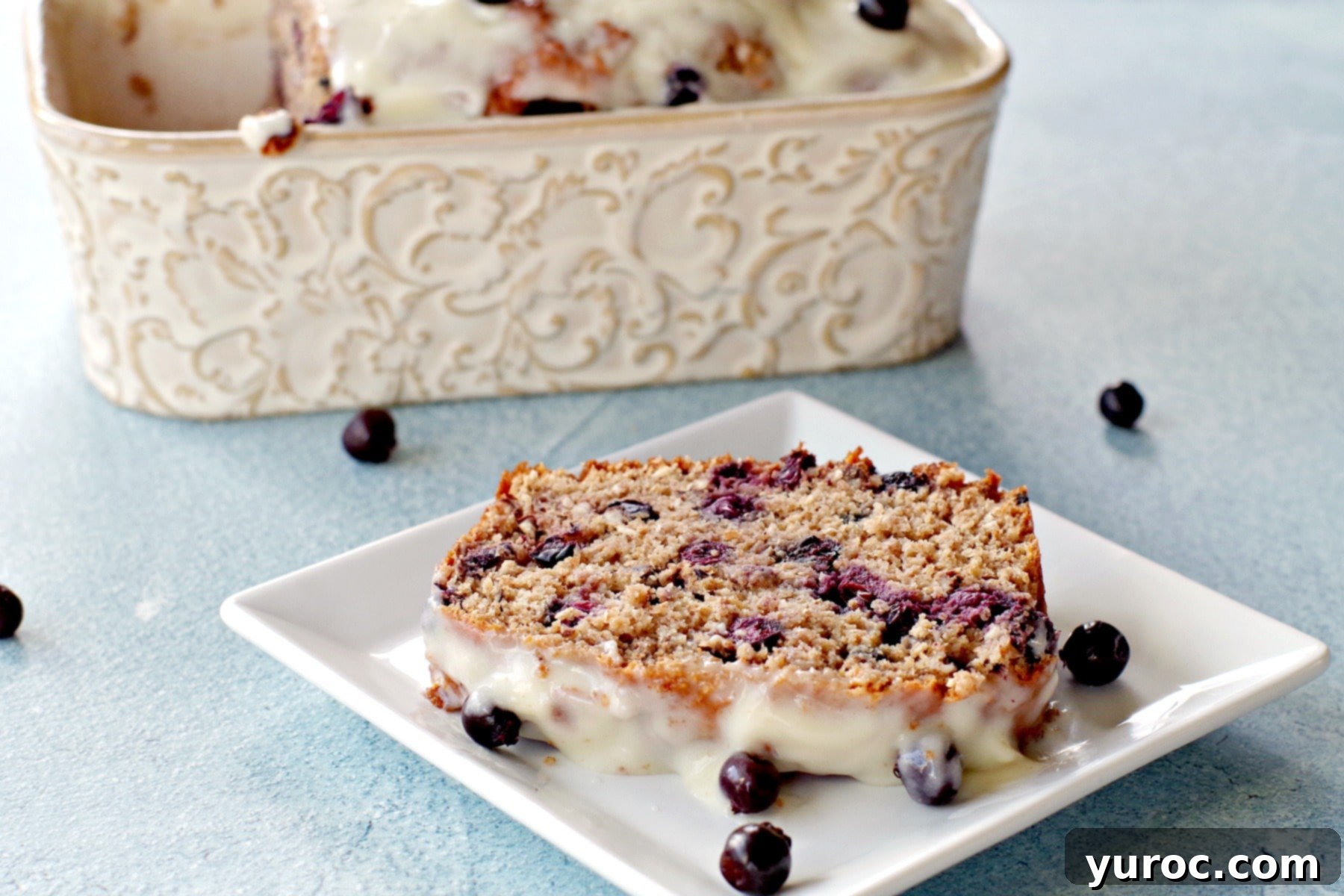 A perfectly baked slice of Saskatoon berry loaf on a white plate, with a loaf pan visible in the background