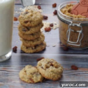 Two soft and chewy oatmeal raisin cookies, one resting partially on the other, with a glass of milk, a stack of more cookies, and a jar of brown sugar in the background.