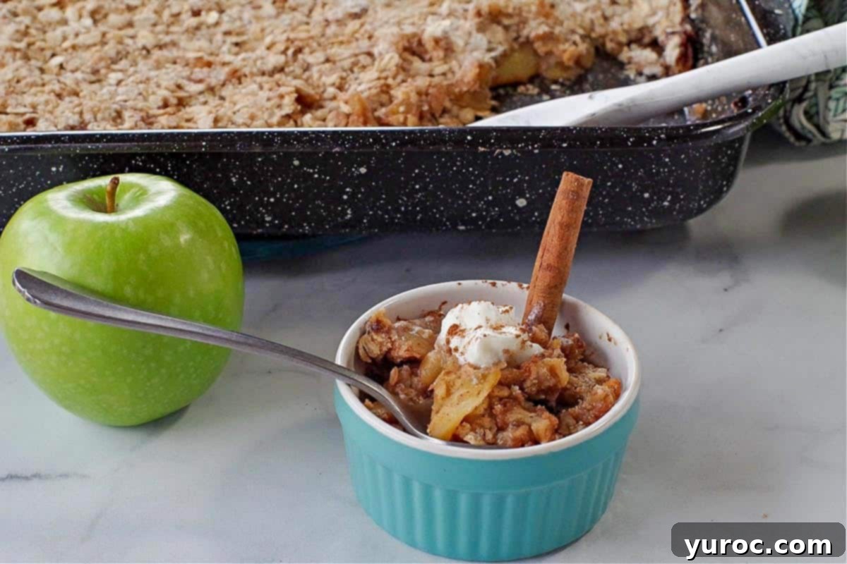 ww apple crisp in a small blue dish with green apple and pan of more apple crisp in the background