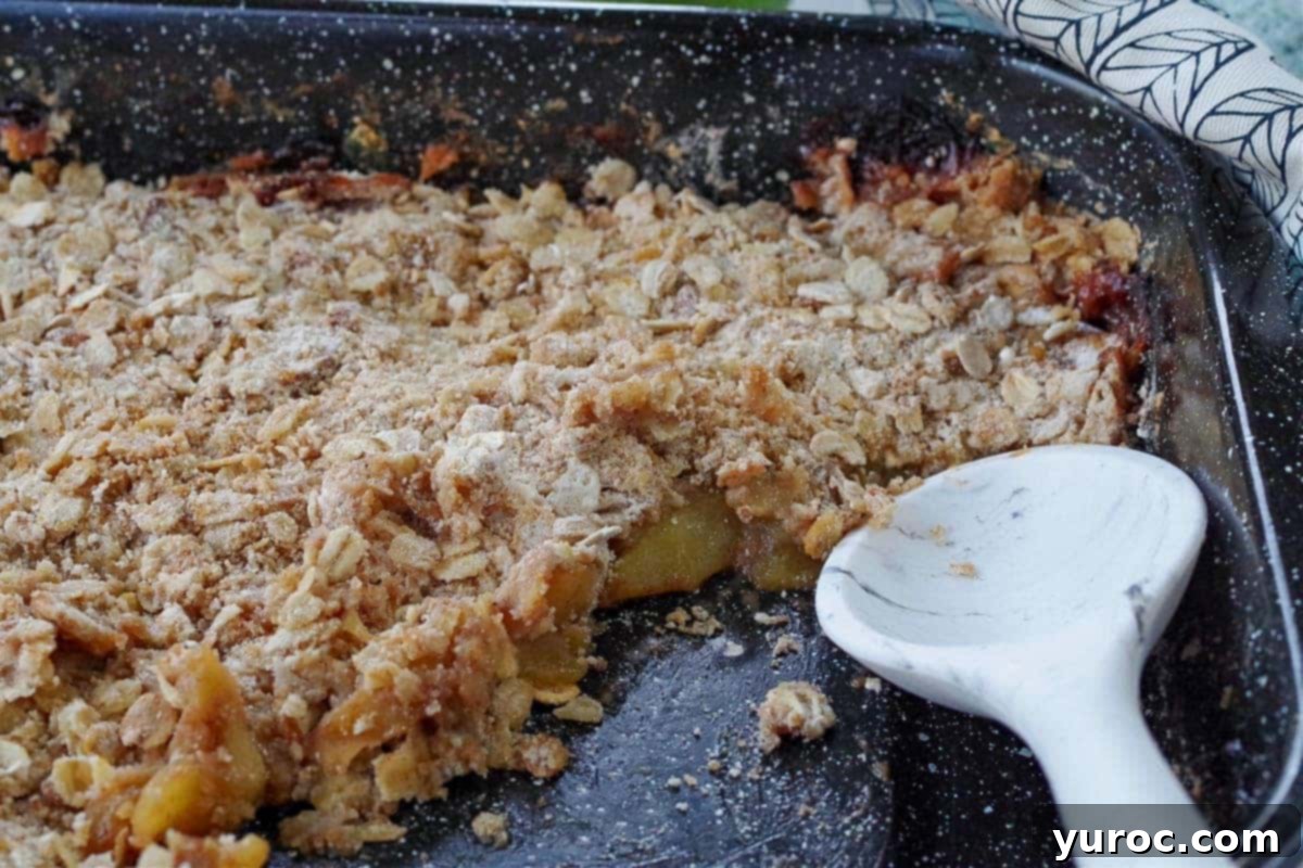 WW apple crisp in a pan with some missing and a white marbled silicone spoon.