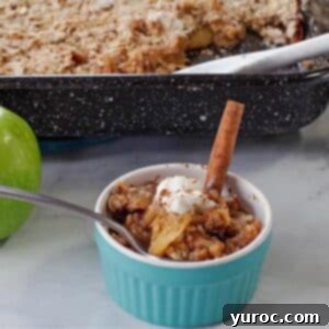 ww apple crisp in a small blue dish with green apple and pan of more apple crisp in the background