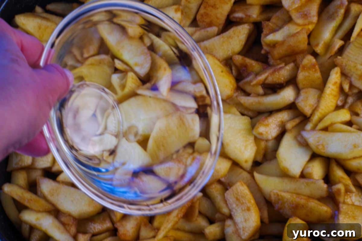 Water being poured over apples in a prepared baking dish