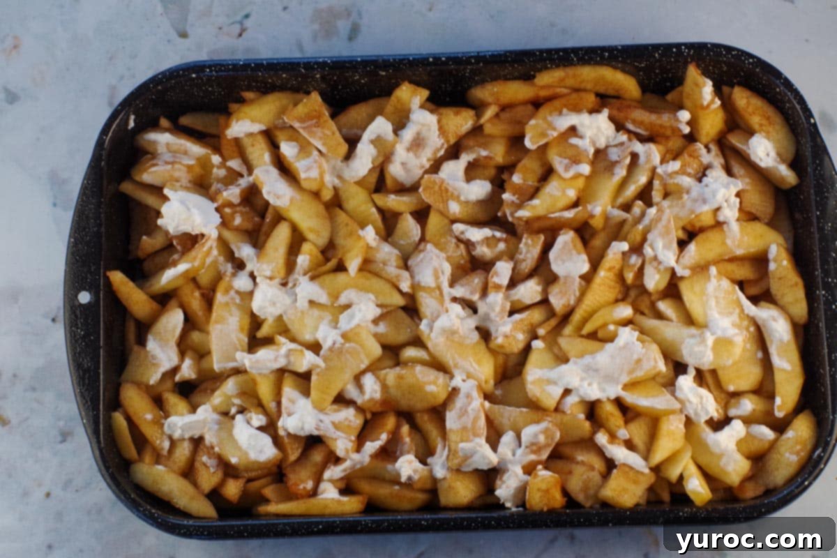 Whipped cream spread over apple mixture in pan.