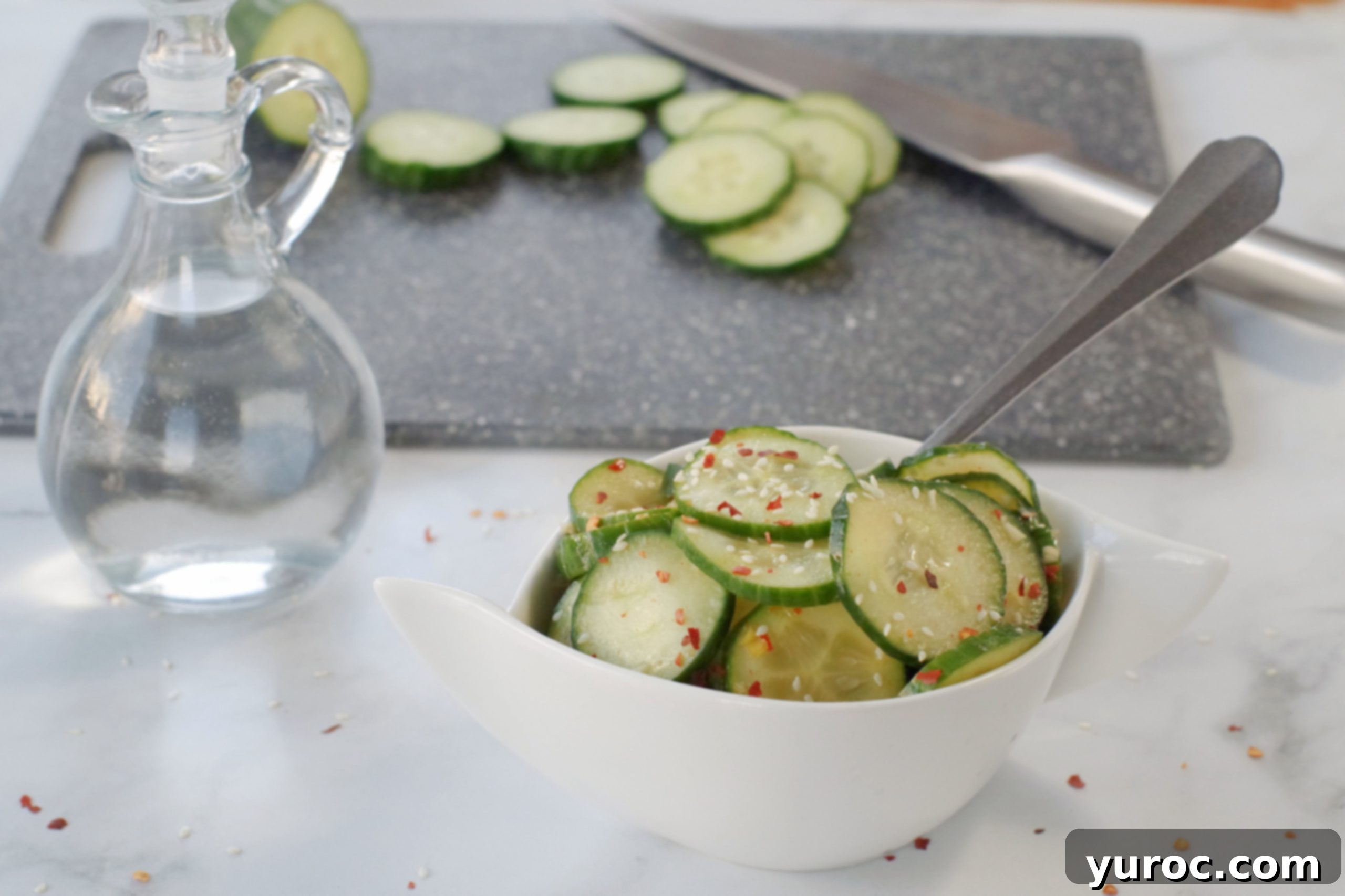 Instant Cucumber Kimchi 3 Quick Kimchi on grey marble counter surface with glass vinegar container in background as well as a grey cutting board with sliced cucumbers and a knife