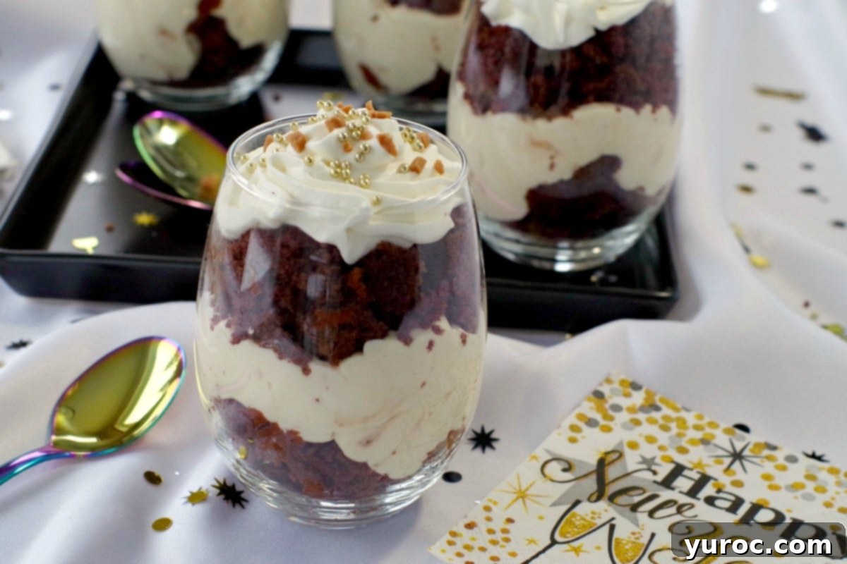 Two mini eggnog trifles in glass bowls, garnished with edible gold candy pearls, surrounded by elegant New Year's Eve decorations and festive napkins. Three more trifles are blurred in the background on a black tray, creating a luxurious holiday atmosphere.
