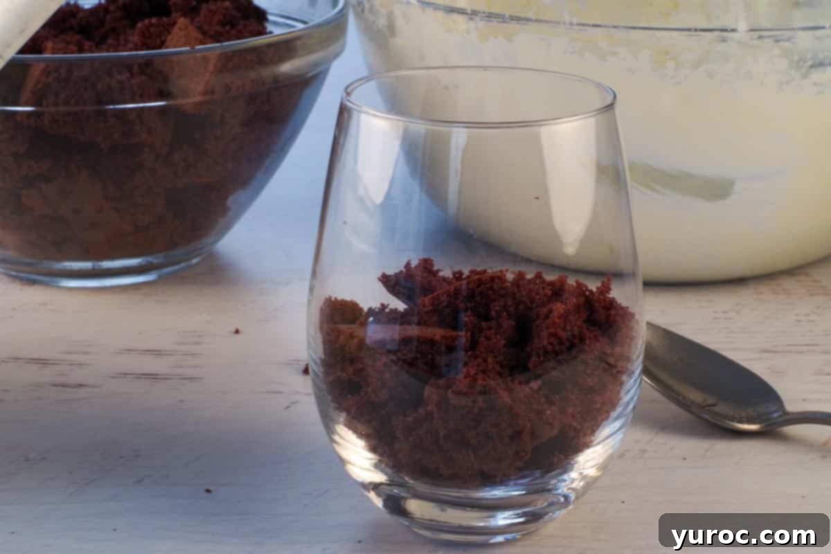 The initial layer of cubed chocolate cake perfectly placed at the bottom of a clear glass, forming the base for the mini eggnog trifle.