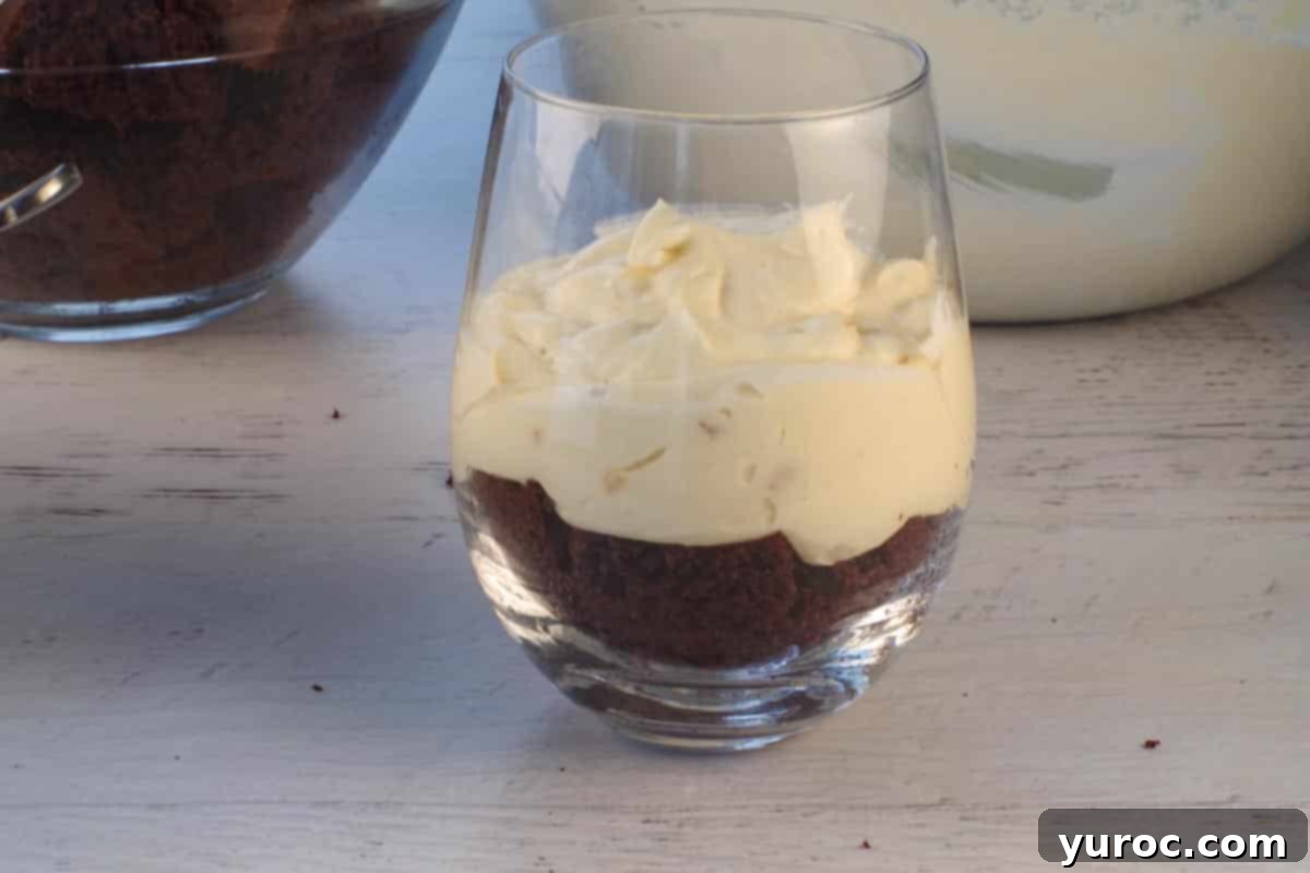 The creamy eggnog pudding mixture being carefully added as the second layer, directly over the chocolate cake base in a glass, creating a distinct visual layer.