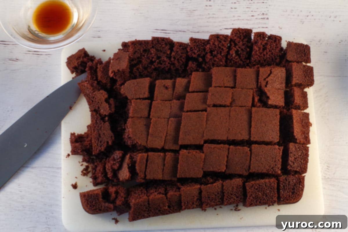 Chocolate cake, freshly cut into uniform ½-1 inch cubes, neatly arranged on a wooden cutting board next to a sharp knife, ready for layering.