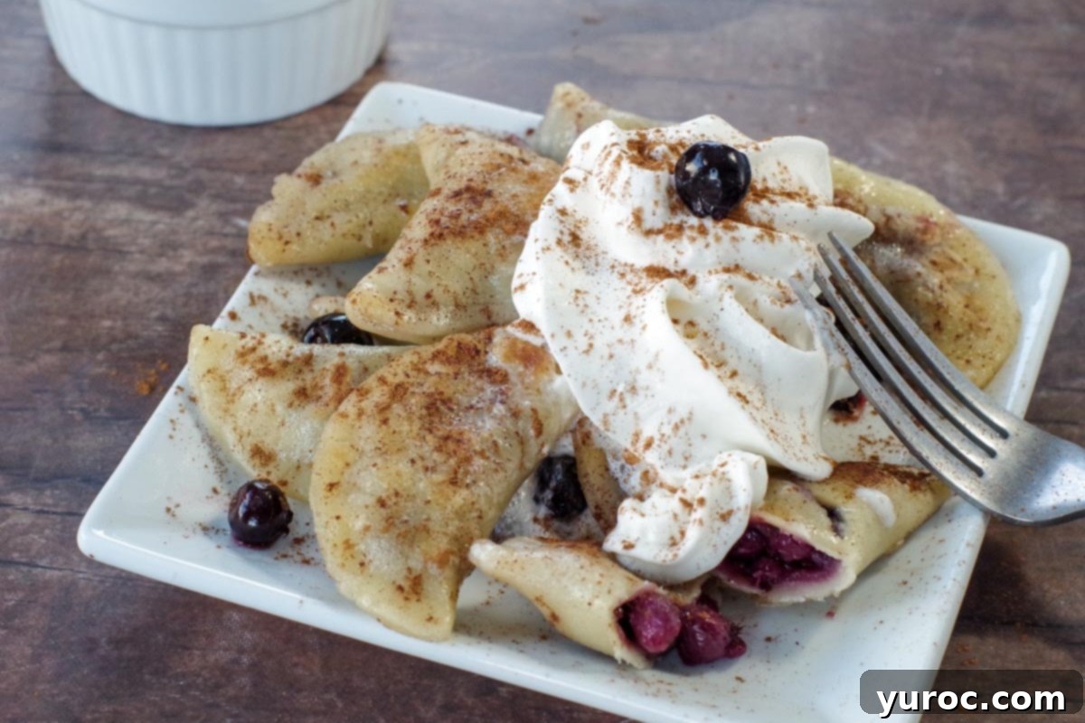 Saskatoon berry dessert pierogies on a white plate with a fork, garnished with whipped cream and cinnamon