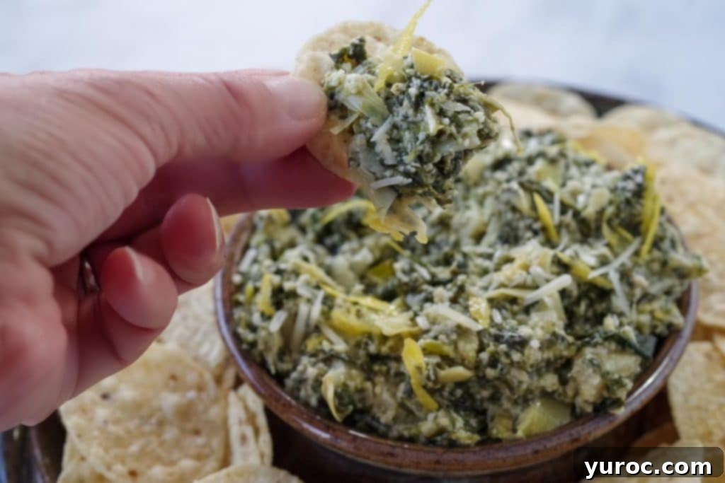 Guilt Free Greek Yogurt Spinach Artichoke Dip 3 spinach artichoke dip being held up on a chip over a platter of more dip and tortilla chips