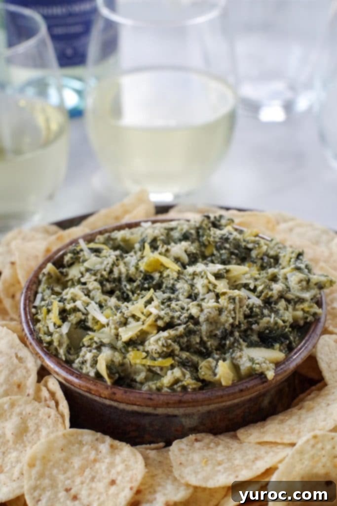 Guilt Free Greek Yogurt Spinach Artichoke Dip 4 spinach artichoke dip on a platter with glasses of wine in the background