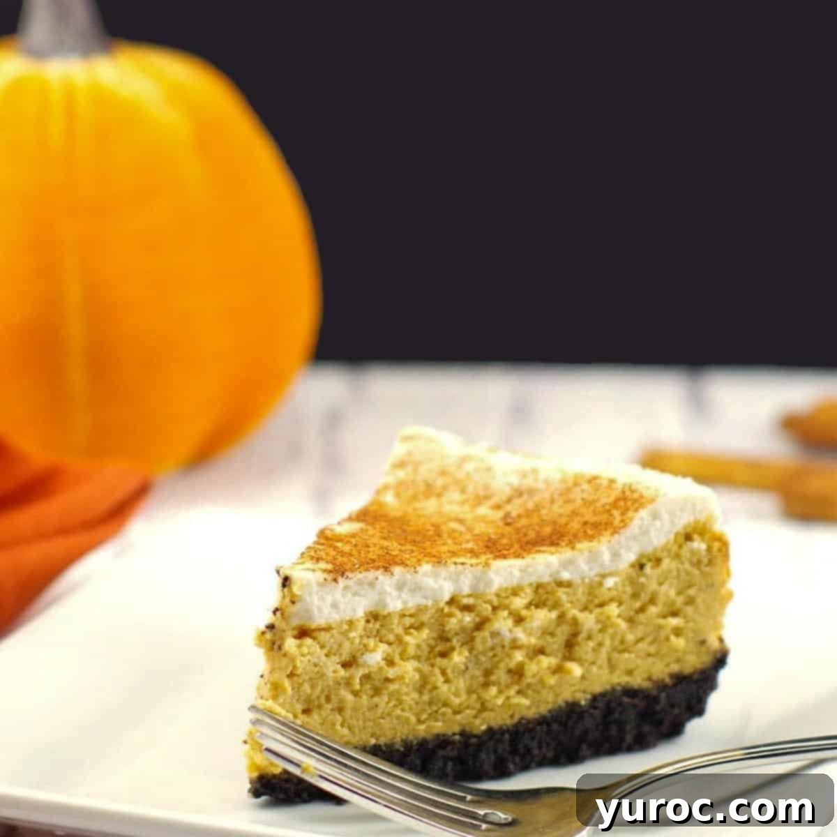 Light Pumpkin Oreo Cheesecake 10 A perfectly sliced piece of light pumpkin cheesecake on a white plate, with a fork, and a decorative stuffed pumpkin in the background.