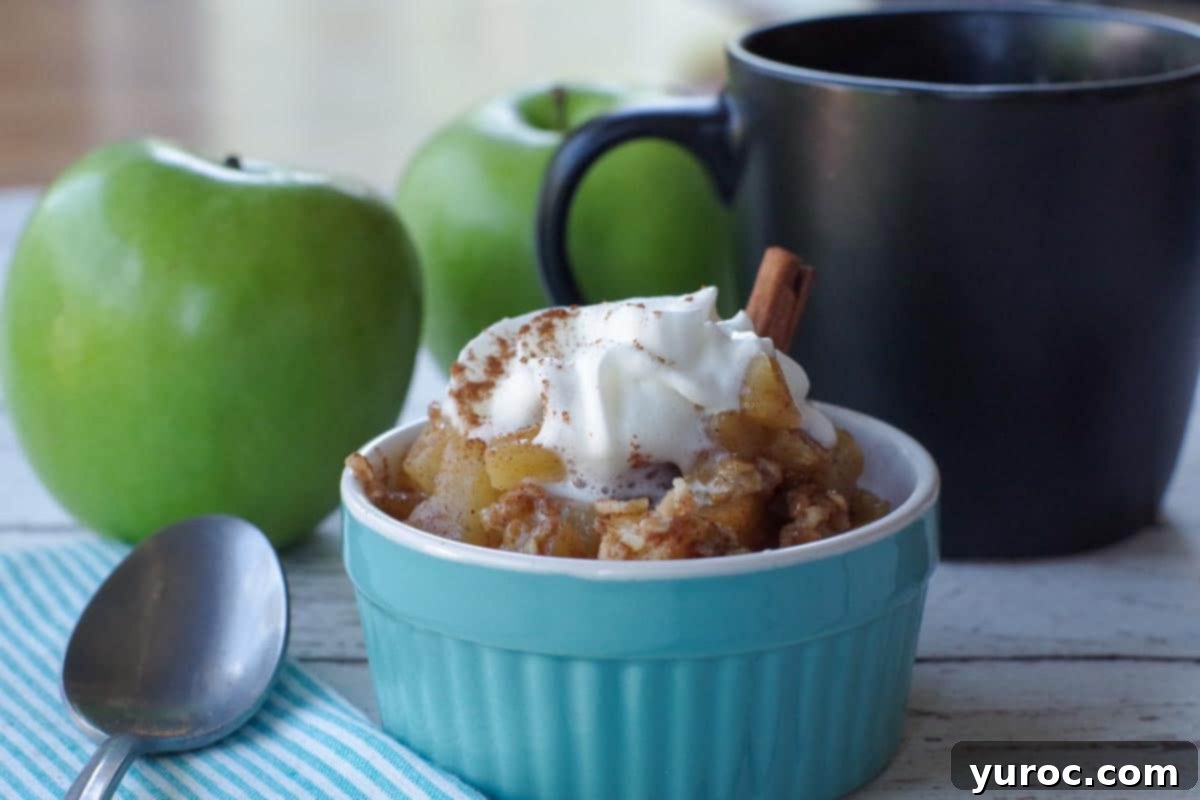 mug apple crisp in a blue dish with black mug and 2 green apples in the background