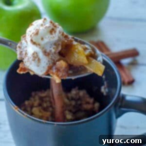 spoon with apple crisp being held up above a black mug apple crisp with 2 green apples and cinnamon sticks in the background