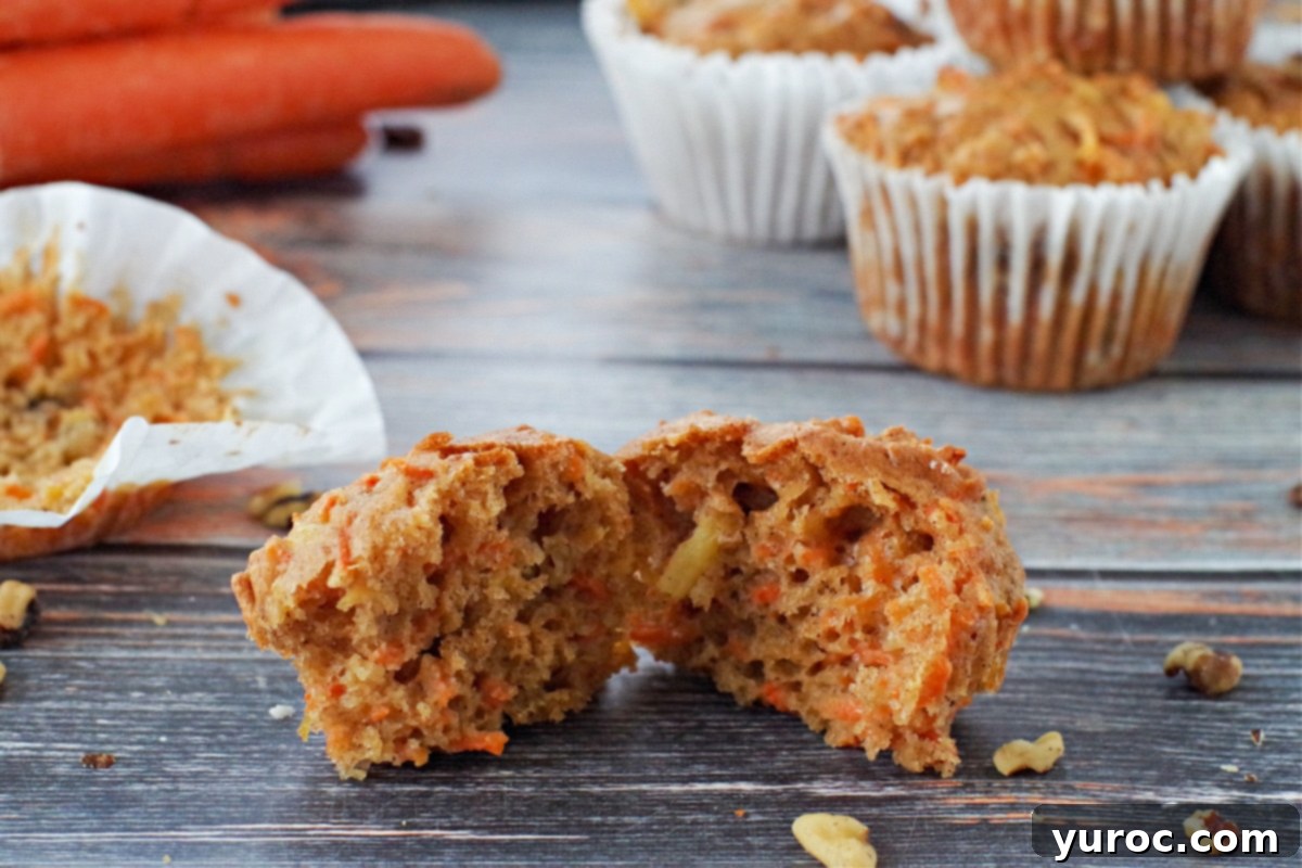 Sunshine Carrot Pineapple Muffins 2 Two healthy carrot muffins with pineapple, one split open, on a blue wood-like surface. More muffins and fresh carrots are blurred in the background, hinting at wholesome ingredients.