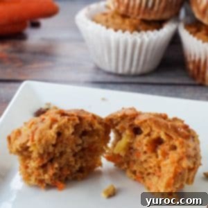 Sunshine Carrot Pineapple Muffins 10 A healthy carrot muffin with pineapple, split in half, showcasing its moist interior with visible carrot shreds and nuts. It sits on a blue wood surface, surrounded by other muffins and fresh carrots.