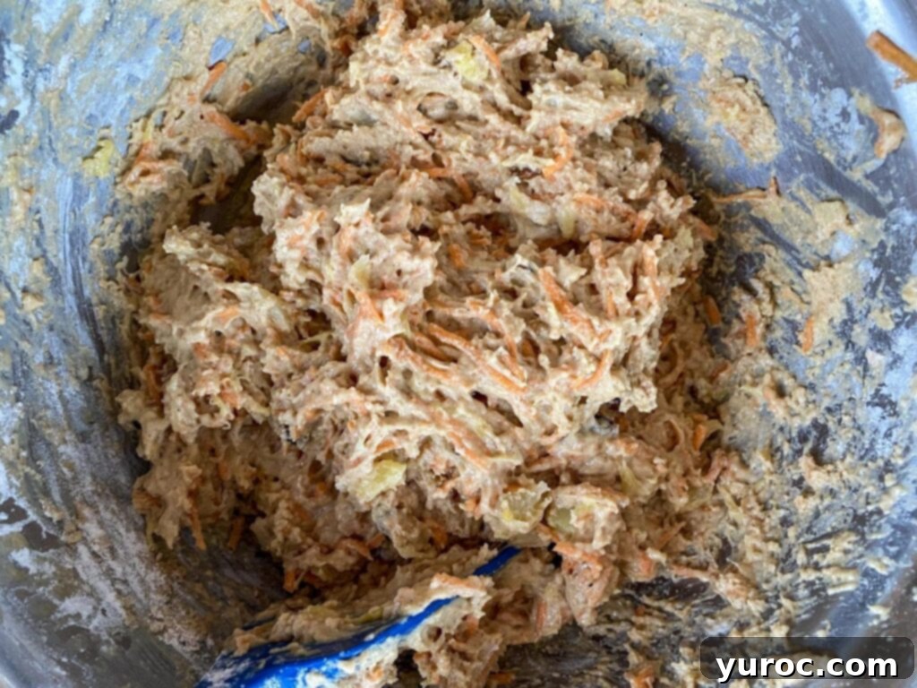 Sunshine Carrot Pineapple Muffins 6 Dry ingredients combined with wet ingredients in a large bowl, being gently stirred to form a cohesive muffin batter.
