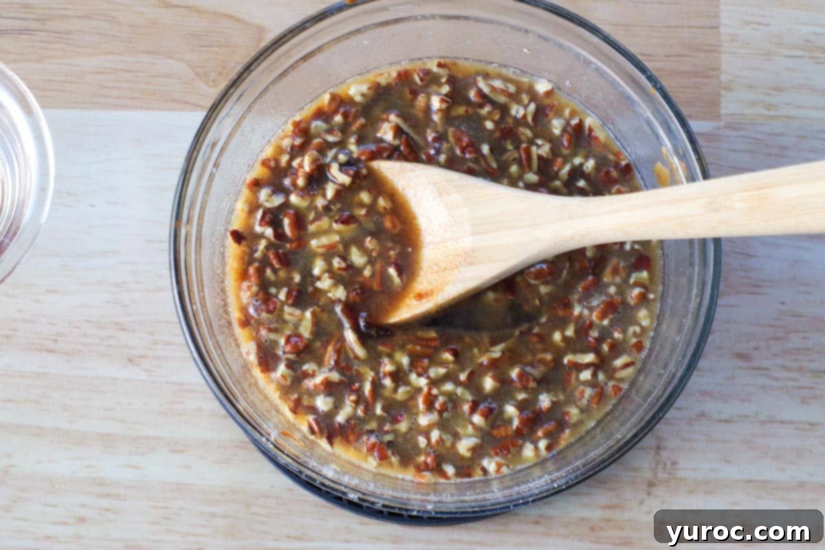Pecans and vanilla extract added to mixture in glass bowl with wooden spoon