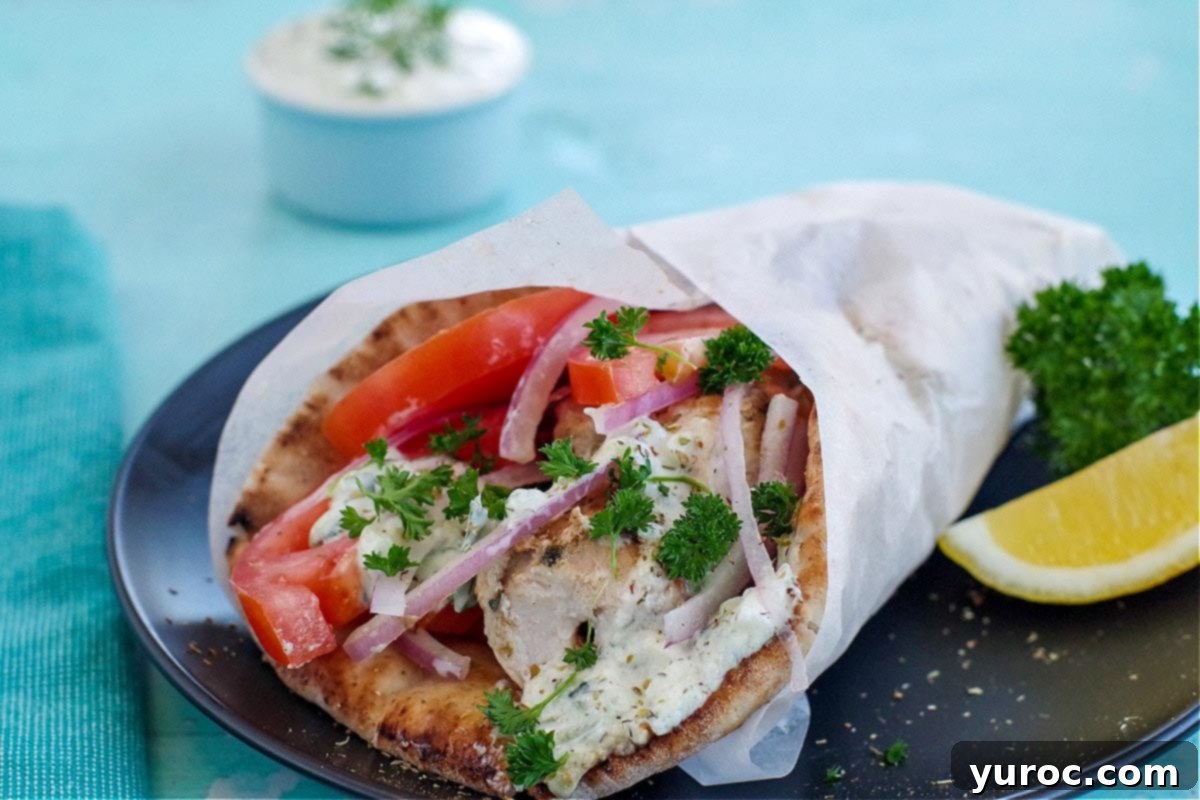 Greek chicken souvlaki wrapped in pita with tomatoes, red onion, tzatziki and parsley, wrapped in paper on black plate