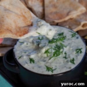 triangle of pita bread being dipped into tzatziki sauce in black bowl on black tray with pita bread in background and lemon wedges
