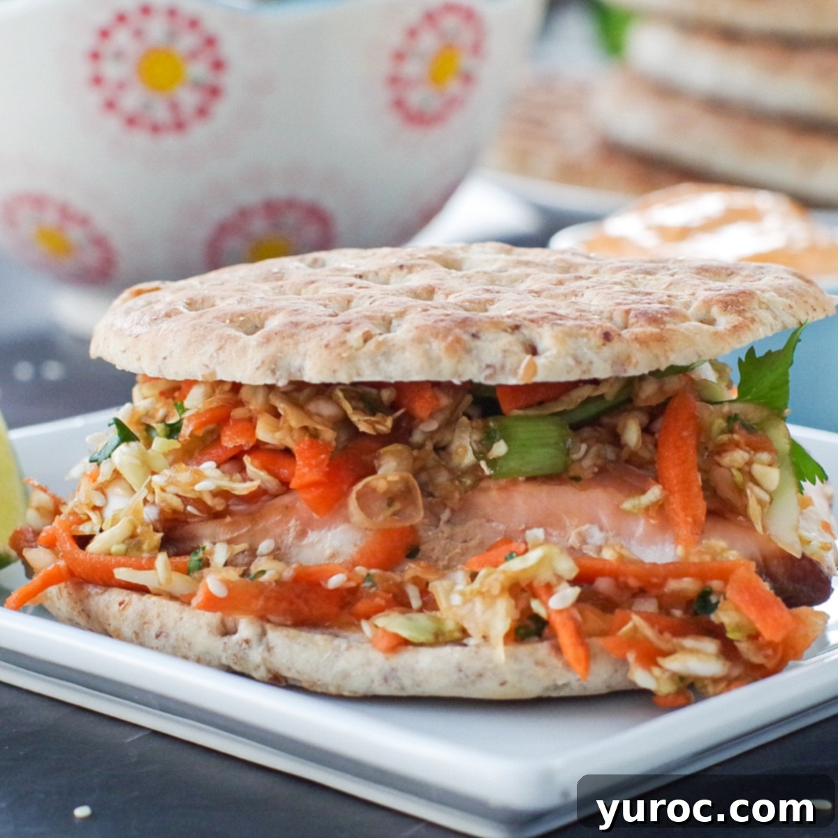 Delicious air fryer salmon burger served on a white plate with a side of creamy coleslaw, with burger buns and spicy sriracha mayo in the background, ready to be assembled.