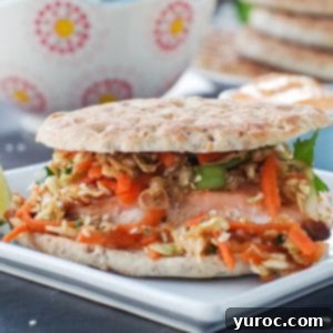 salmon burger on white plate with coleslaw, buns on a plate and sriracha mayo in background