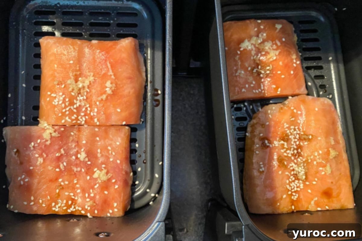Four frozen salmon fillets neatly arranged in the two drawers of an air fryer, ready for cooking.