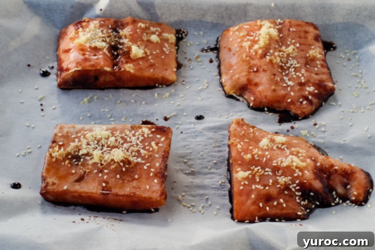 Close-up of frozen salmon fillets seasoned with soy sauce, fresh ginger, and sesame seeds, illustrating the preparation before cooking.