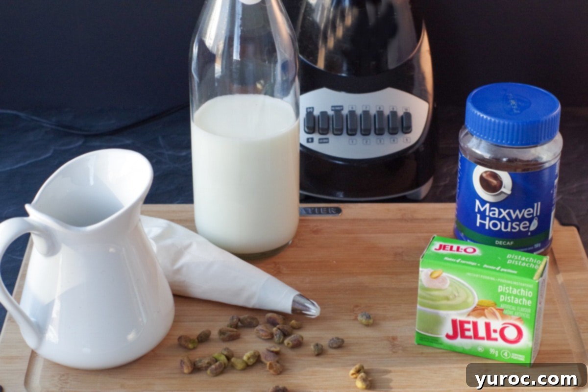 Barista-Style Pistachio Frappe 4 ingredients for pistachio frappuccino on cutting board with blender in background
