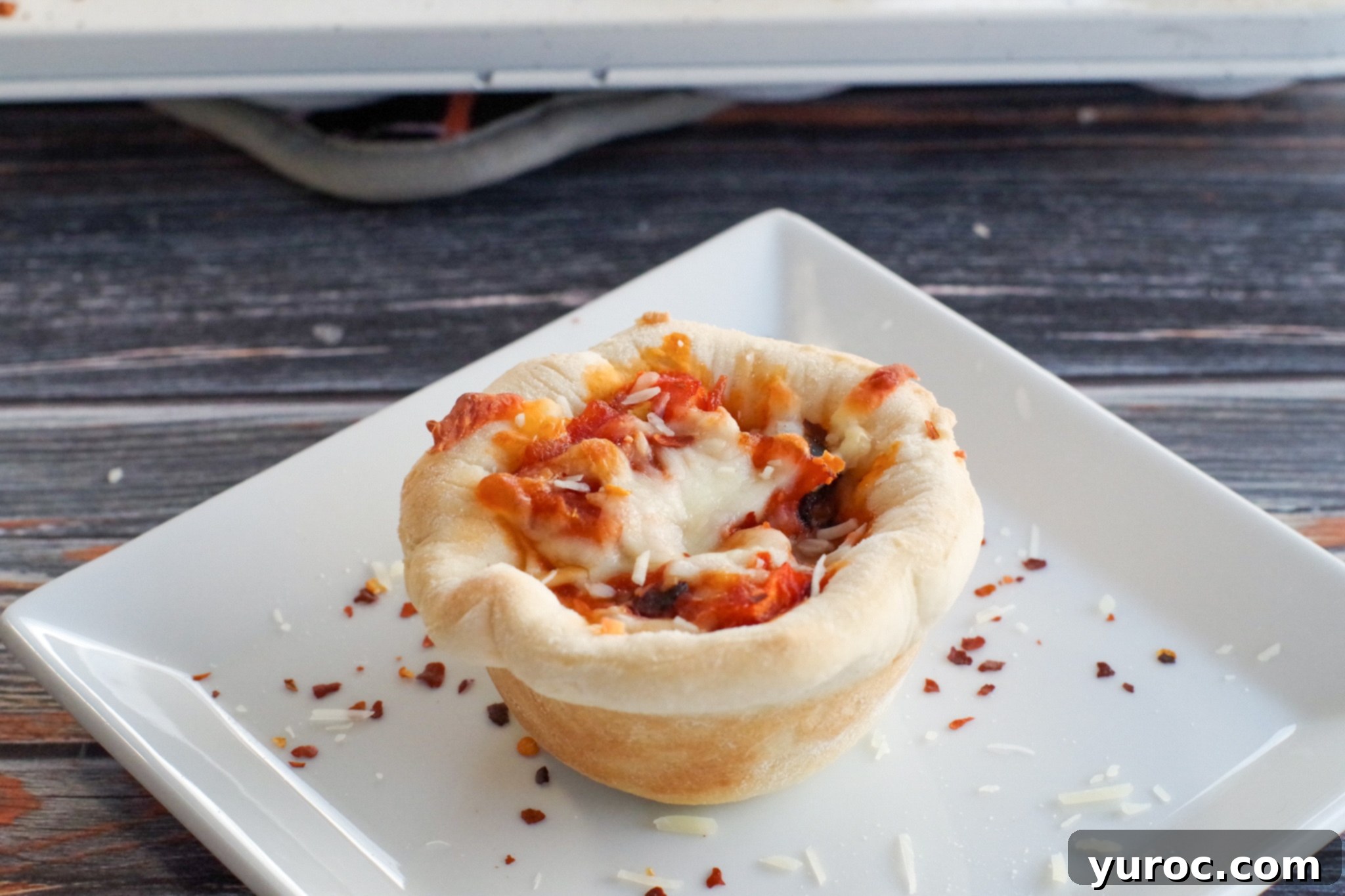 Delicious bacon and red onion pizza cupcake served on a white plate with crushed red pepper and parmesan cheese sprinkles