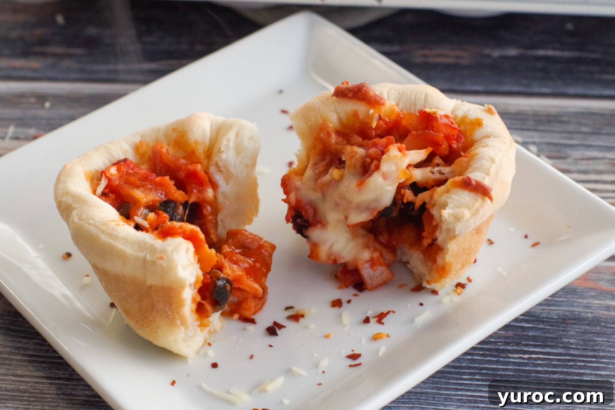 A freshly baked pizza cupcake sliced in half, revealing a rich filling of bacon, red onion, and melted cheese, served on a white plate with red pepper flakes