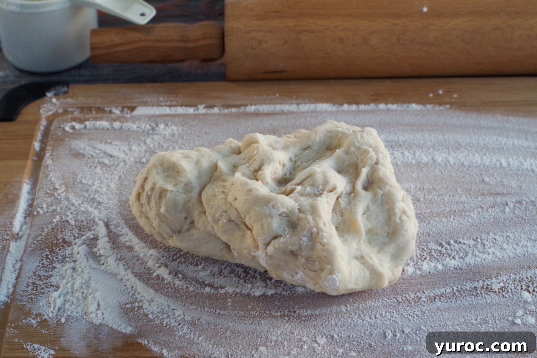 Pizza dough resting on a lightly floured surface, with a rolling pin visible in the background