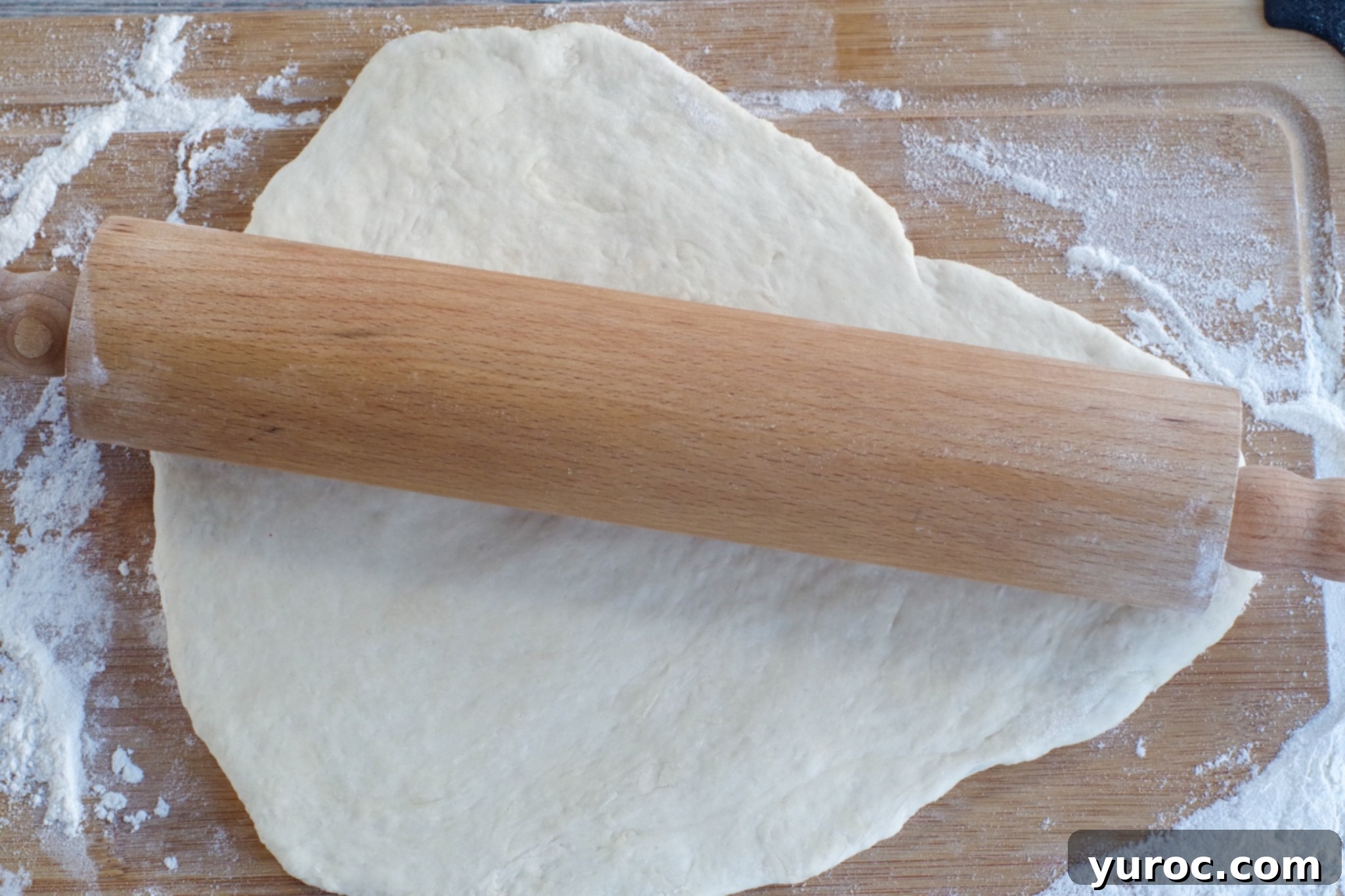 Pizza dough evenly rolled out on a wooden cutting board, ready for cutting
