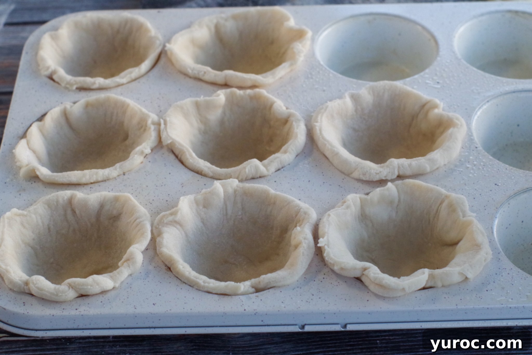 Pizza dough circles neatly pressed into the cups of a muffin tin