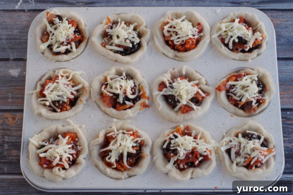 Muffin tin with pizza dough crusts filled with sauce, cheese, and other pizza toppings, ready for baking