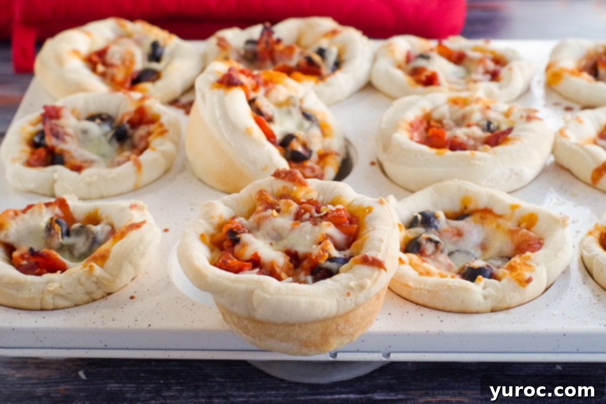 One golden-brown pizza cupcake perfectly removed from a muffin tin, resting on the edge, with other pizza cupcakes still in the tin