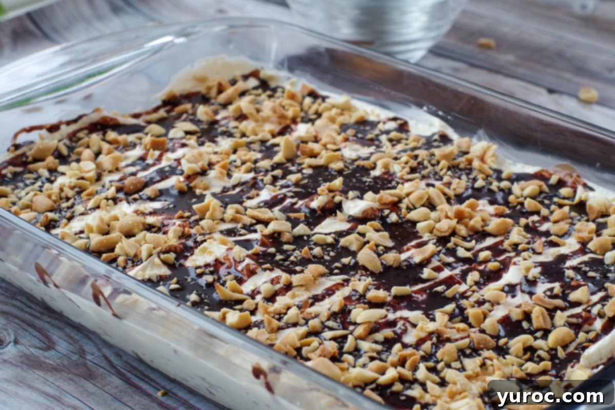 No-Bake Drumstick Dessert in a clear glass pan, showing distinct layers of crunchy crust, creamy filling, and a chocolate-peanut topping on a wooden surface.