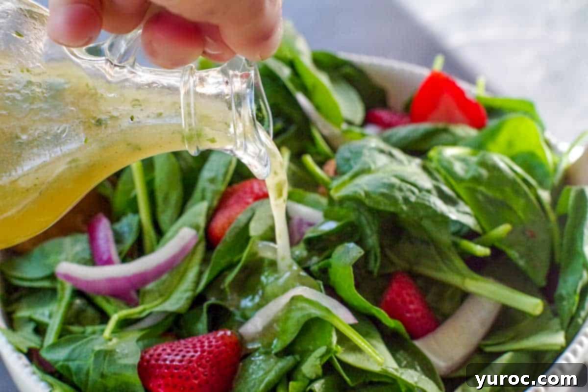 cilantro honey lime dressing being poured onto spinach strawberry pecan salad