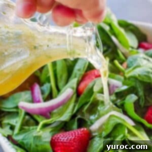 honey lime cilantro vinaigrette being poured over a strawberry spinach salad