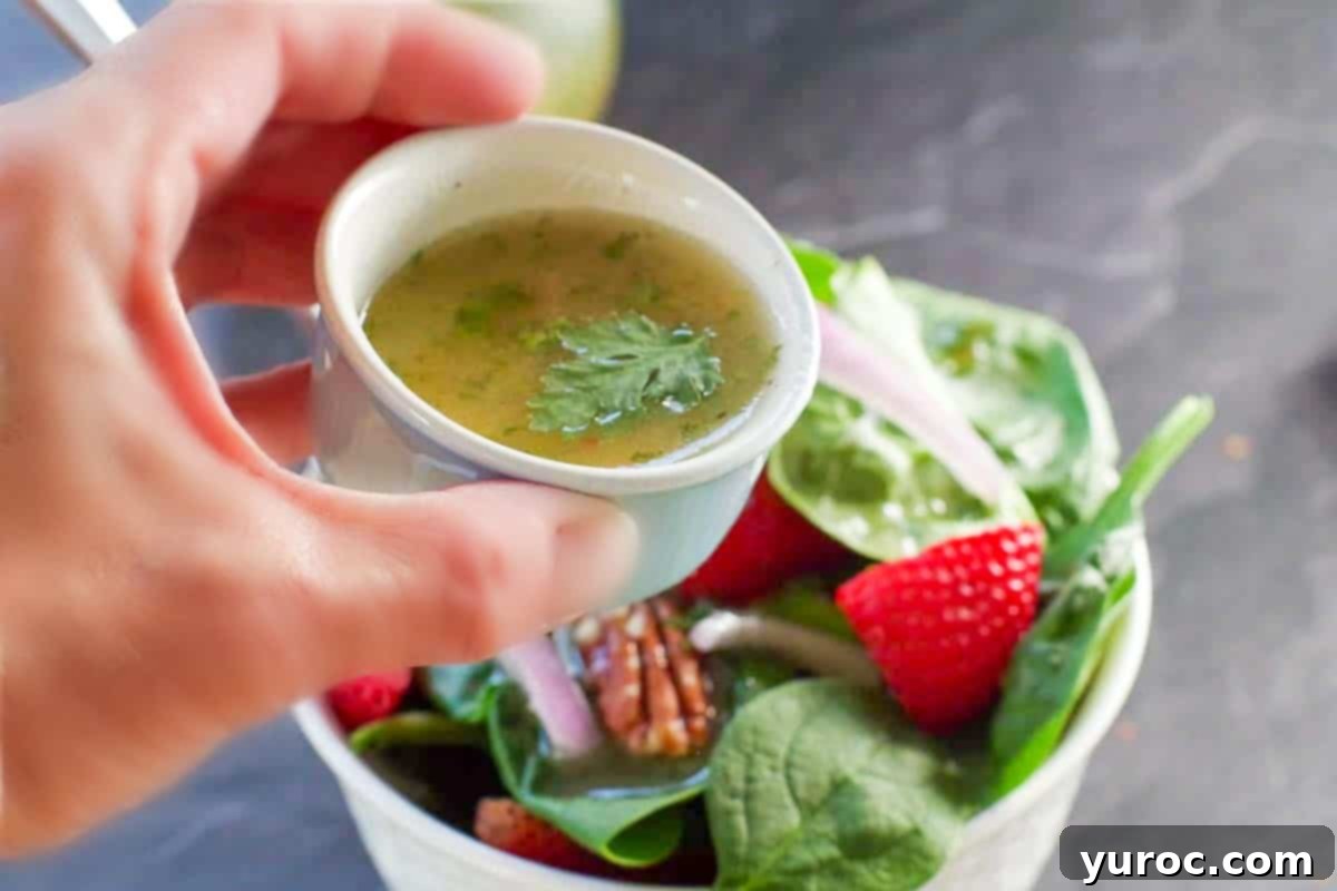 honey cilantro lime dressing in a small blue container being poured over strawberry spinach salad.