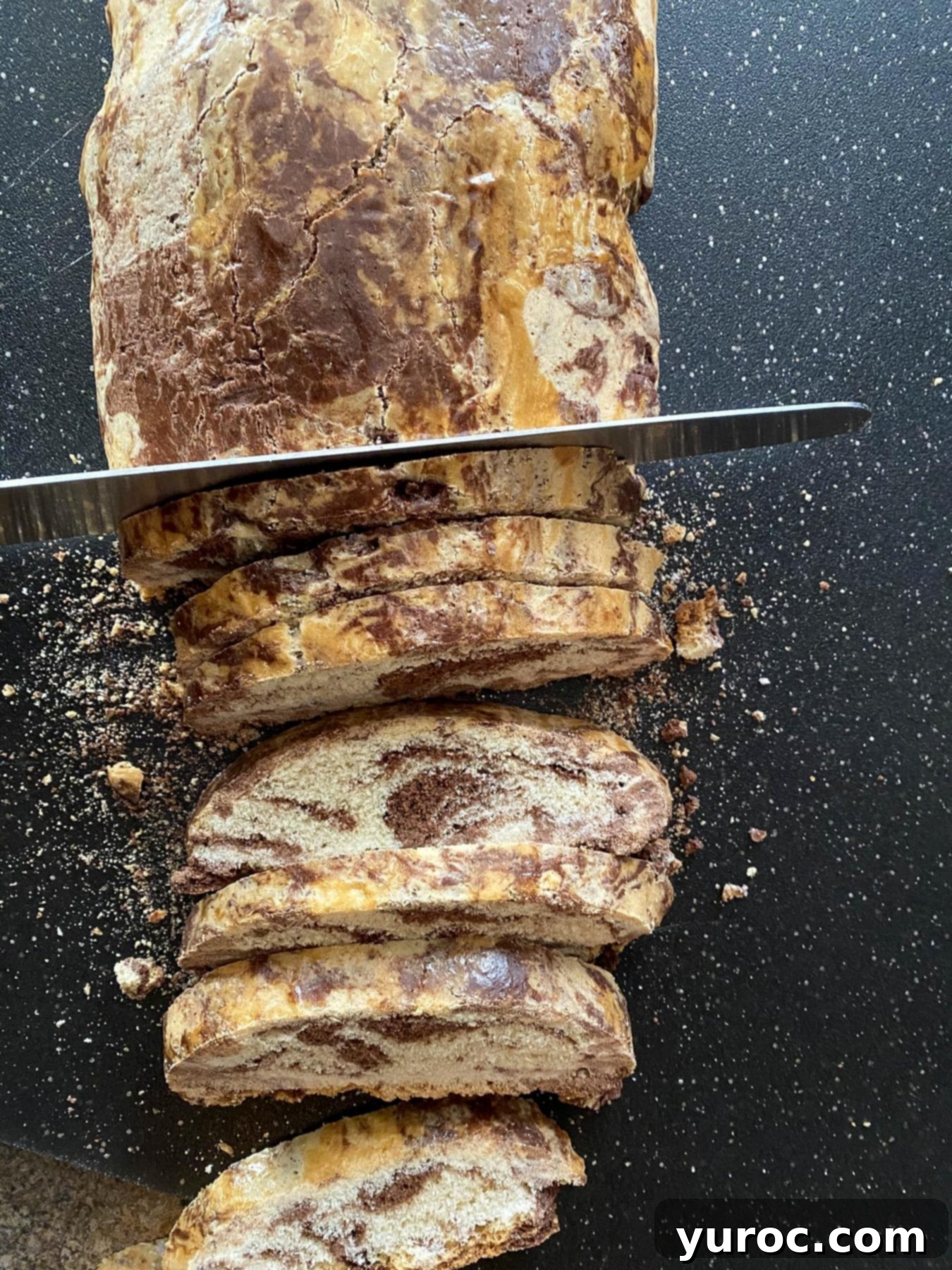 Biscotti being sliced on black cutting board.