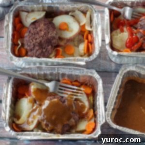 4 hamburger foil packets in aluminum foil containers with potatoes, carrots, onions and hamburgers, on wooden surface