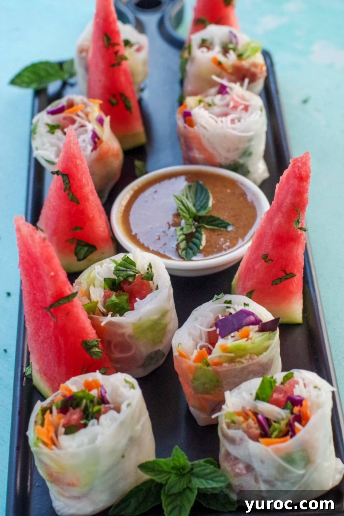 Watermelon Prosciutto Salad rolls, cut in half, on a black platter, with wedges of watermelon