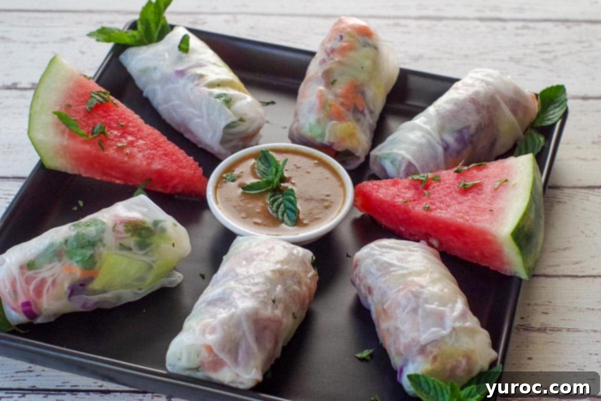 whole salad rolls on a black patter with dip in the middle and watermelon wedges with mint, as garnish