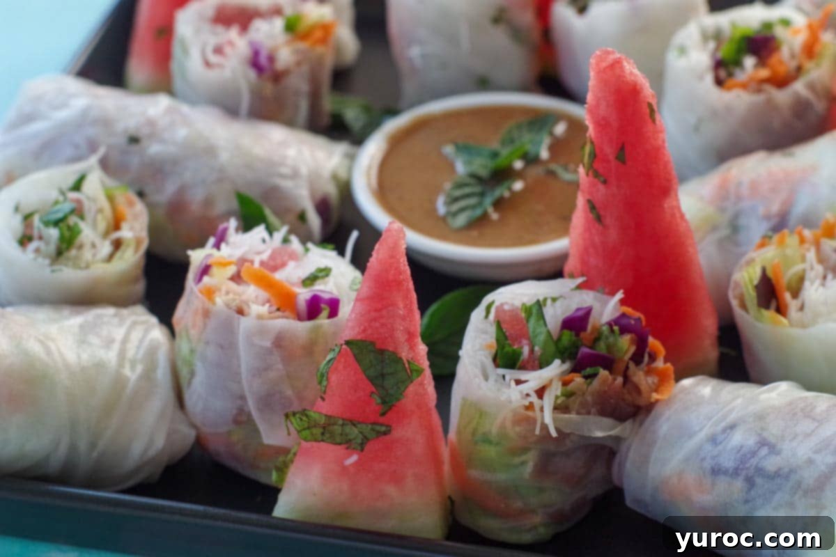salad rolls on a platter, some cut, others whole with dip and wedges of watermelon, sprinkled with fresh mint
