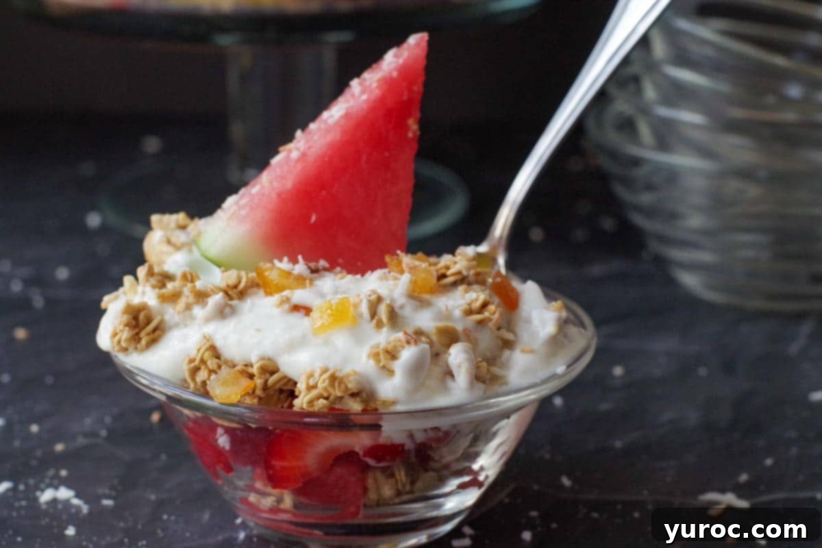 Refreshing Watermelon Granola Parfait 5 watermelon breakfast parfait in a glass bowl with spoon sticking out and more glass bowls in the backgroun