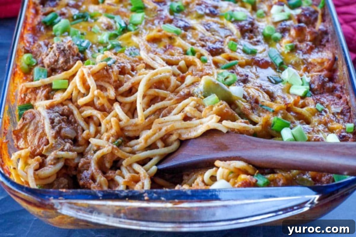 Baked spaghetti casserole in a glass dish with a wooden spoon, ready to be served.